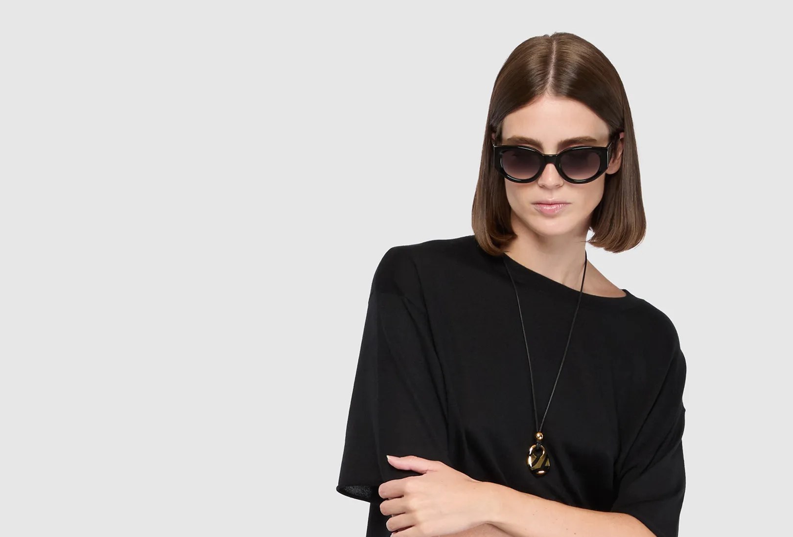 Portrait d’une femme en lunettes de soleil et t-shirt noir, portant un collier pendentif doré et noir