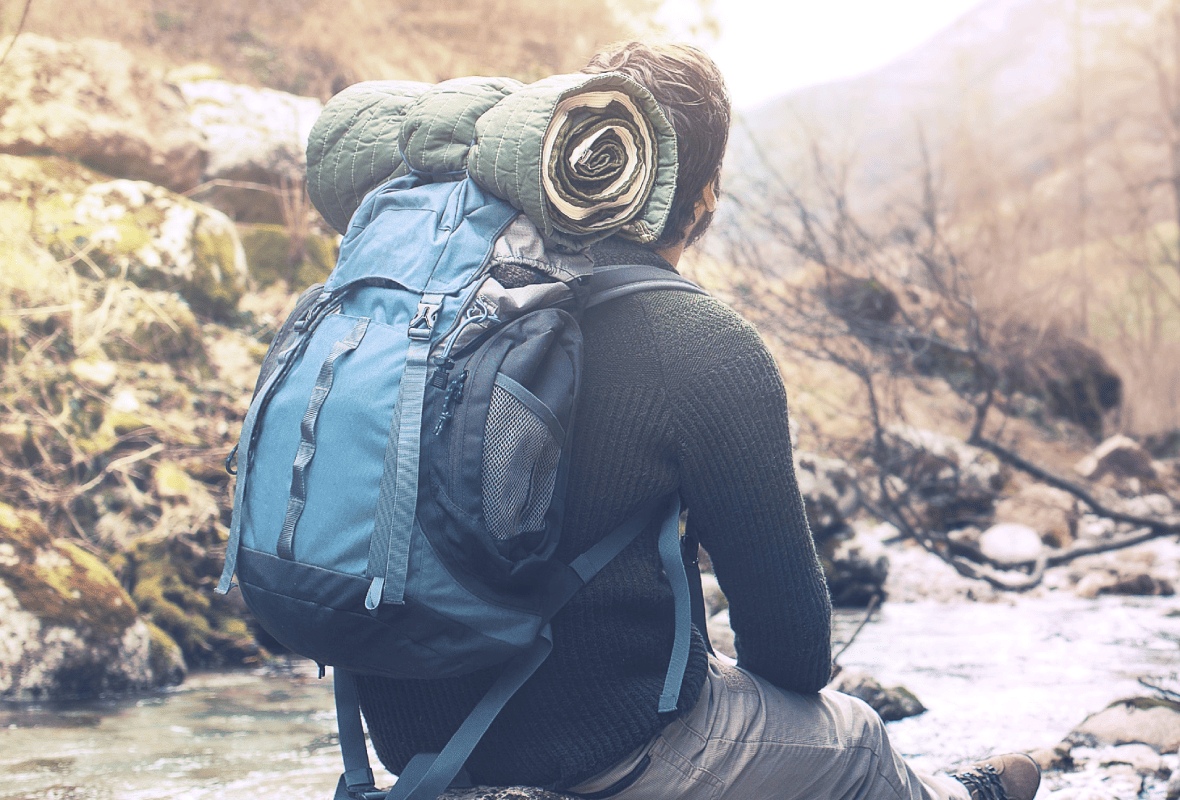 Randonneur de dos au bord d’un ruisseau, sac à dos bleu